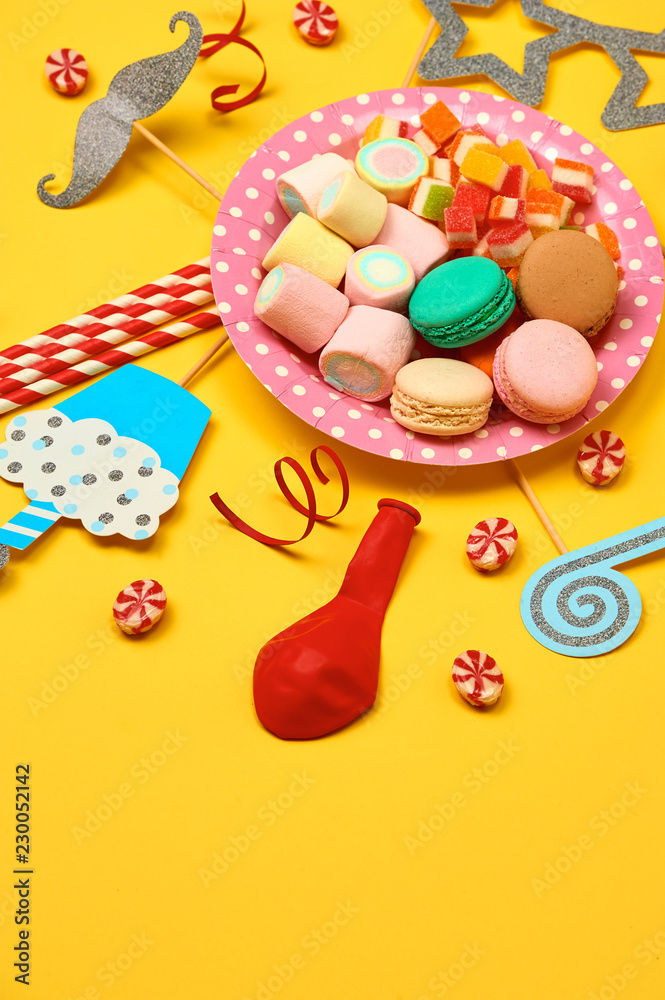 黄色背景的彩色派对、糖果和五彩纸屑俯视模型