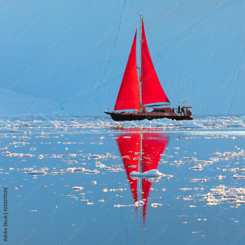 Beautiful red sailboat in the arctic next to a massive iceberg showing the scale. Ilulissat, Disko B