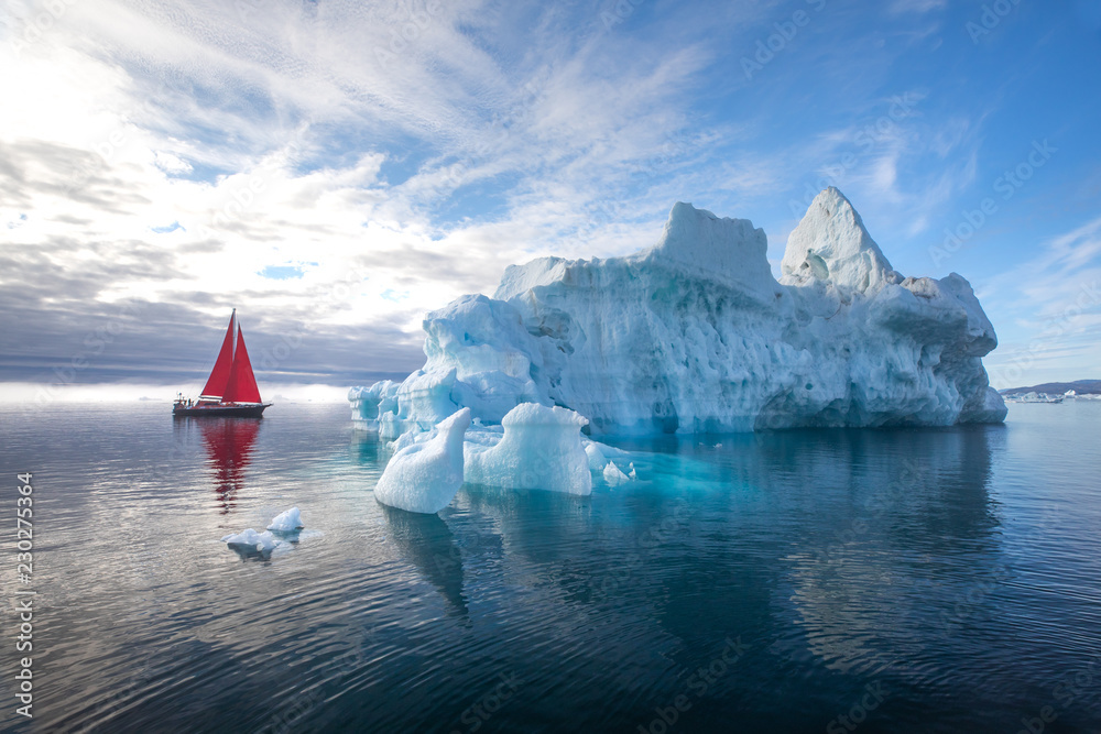 北极美丽的红色帆船，旁边是一座巨大的冰山，展示了其规模。Ilulissat，Disko B