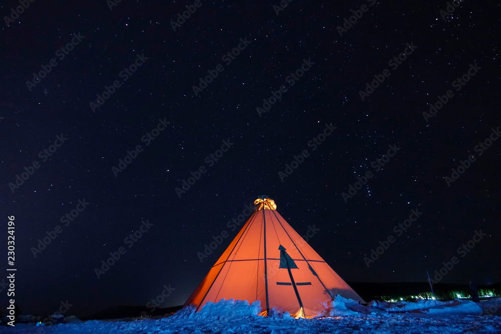 在寒冷的冬夜，橙色发光的帐篷在晴朗的星空下休息。