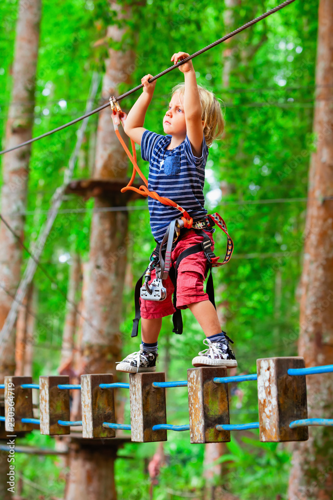 勇敢的孩子戴着安全带爬上树梢，在冒险中通过吊桥障碍物