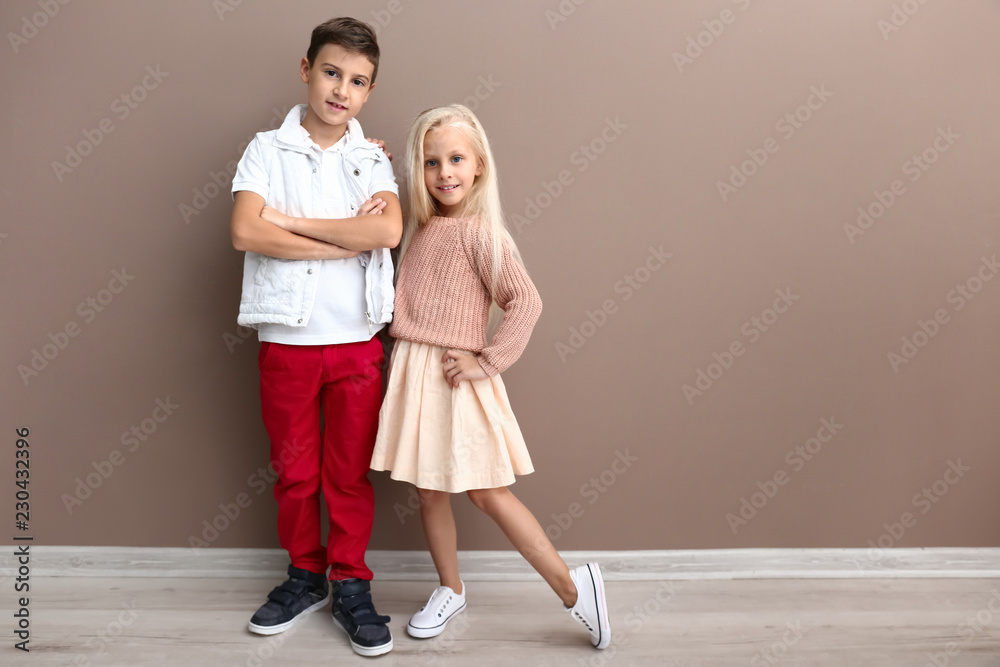 可爱的男孩和女孩穿着时尚的衣服靠近彩色墙
