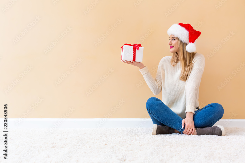 戴着圣诞老人帽的年轻女子在白地毯上拿着一个礼盒
