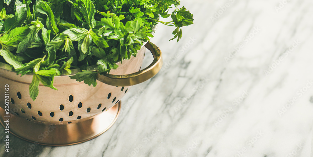 大理石餐桌上方的黄铜漏勺中的一束新鲜绿色花园香草，俯视图，复制空间，