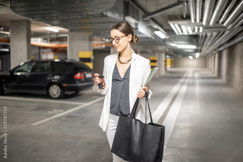 年轻的商务女性拿着车钥匙在新住宅楼的地下停车场行走