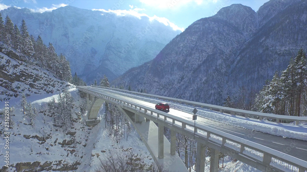 AERIAL红色汽车穿过田园诗般的雪地里建造的混凝土桥