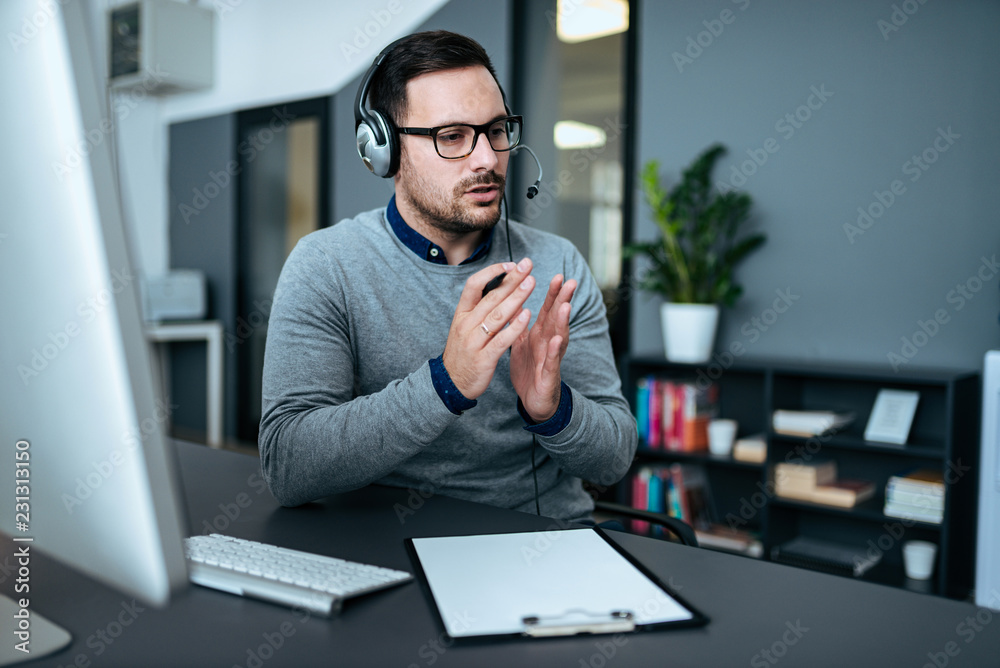 年轻英俊的男性客户支持话务员，戴着耳机在办公室工作。