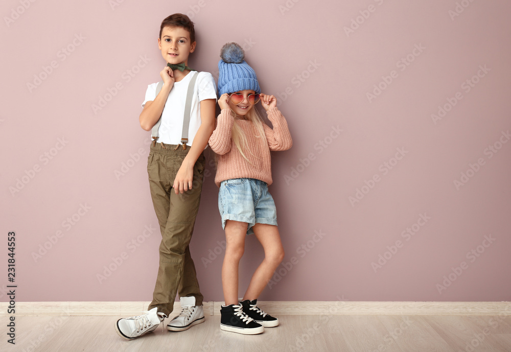 可爱的男孩和女孩穿着时尚的衣服靠近彩色墙