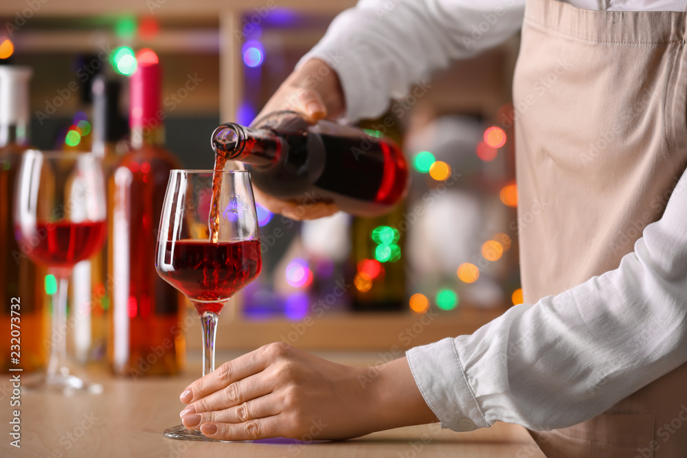 女酒吧男招待将酒瓶中的葡萄酒倒入柜台上的玻璃杯