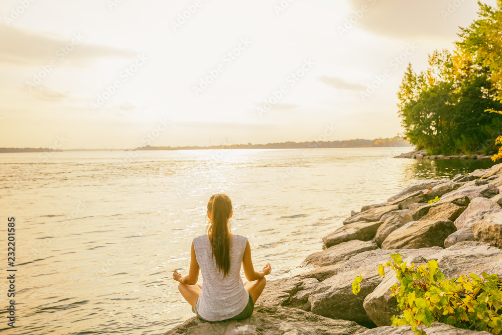 在湖边的自然公园外上瑜伽课。一个女人坐在莲花姿势旁冥想