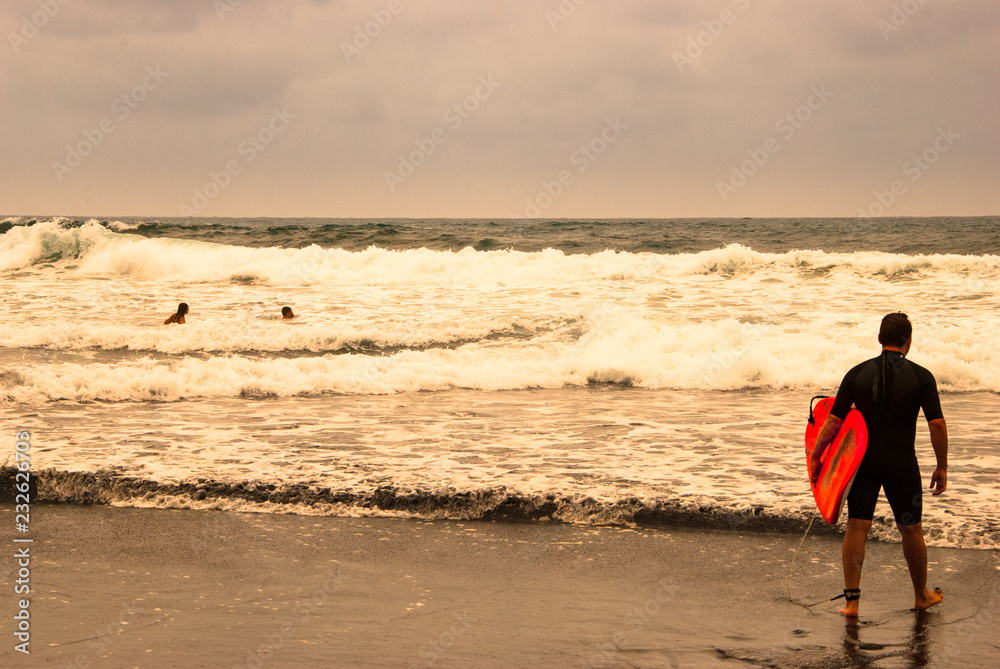 一个拿着红板看海浪的冲浪者