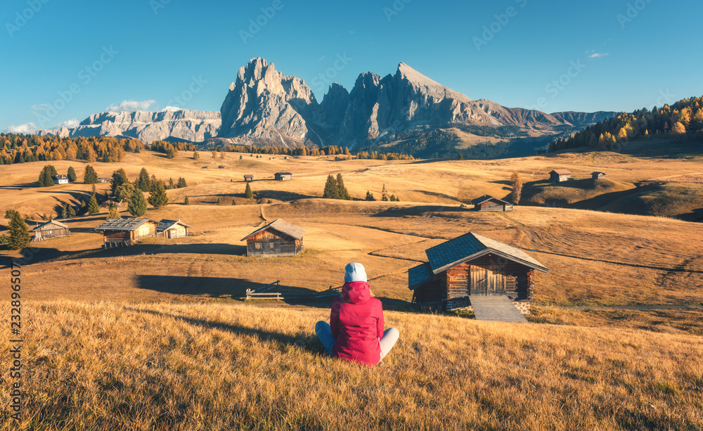 秋天日落时，坐在山上的女人在草地和群山中眺望。多洛姆的阿尔卑斯山