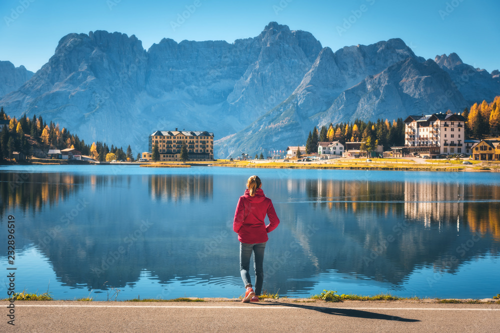 Young woman standing on the coast of Misurina lake at sunrise in autumn. Dolomites, Italy. Landscape