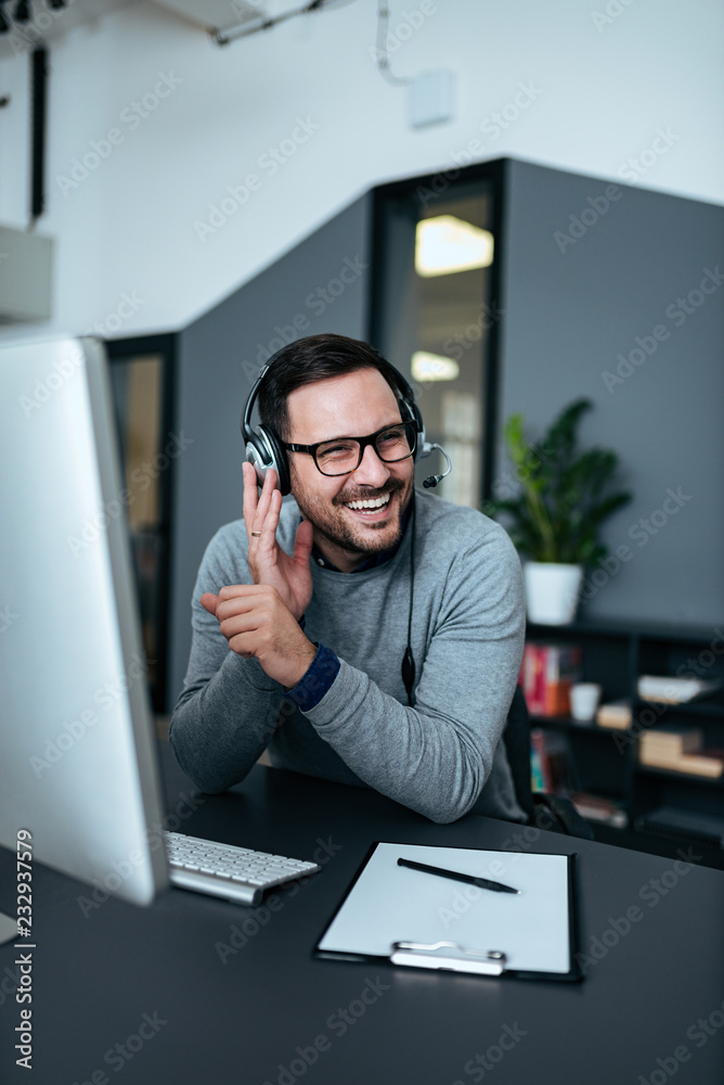 快乐的商人在现代办公室戴着耳机工作。