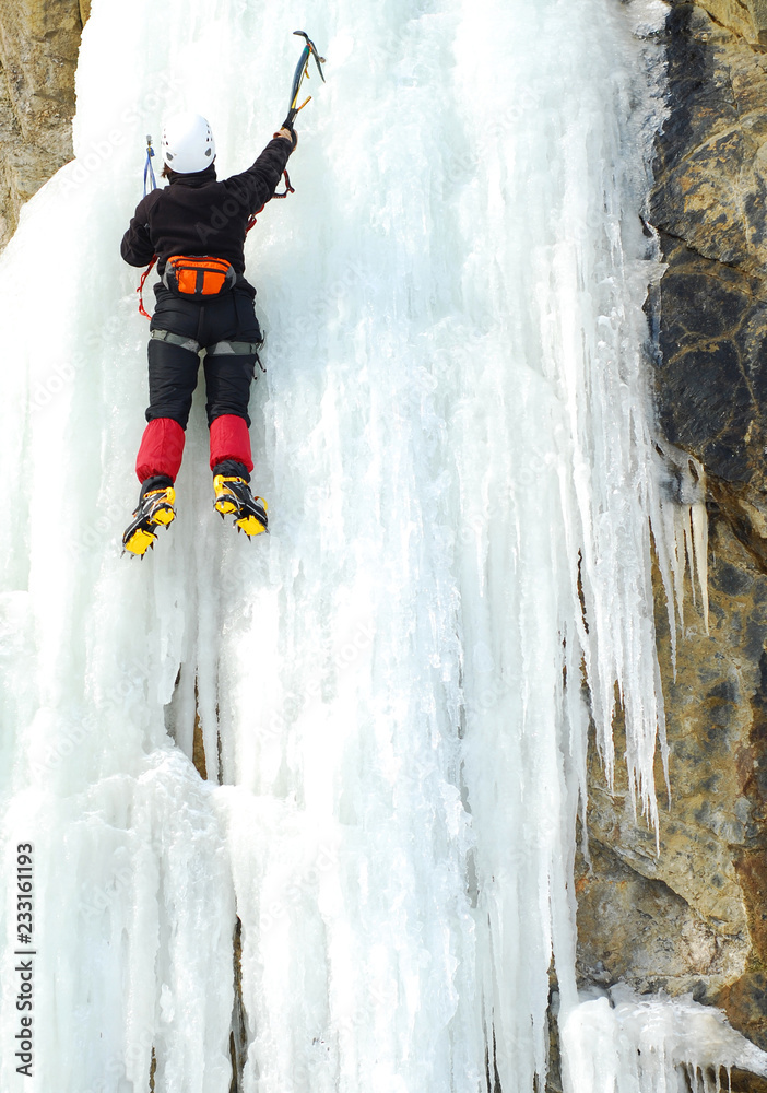 Equipped woman climber ascent by frozen waterfall with climbing using ice axes 