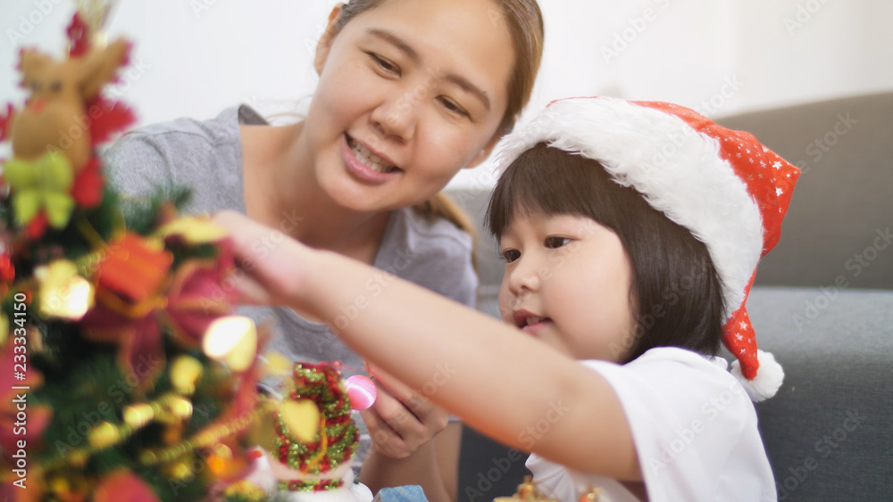 快乐可爱的亚洲女孩和妈妈一起在圣诞树上装饰装饰品