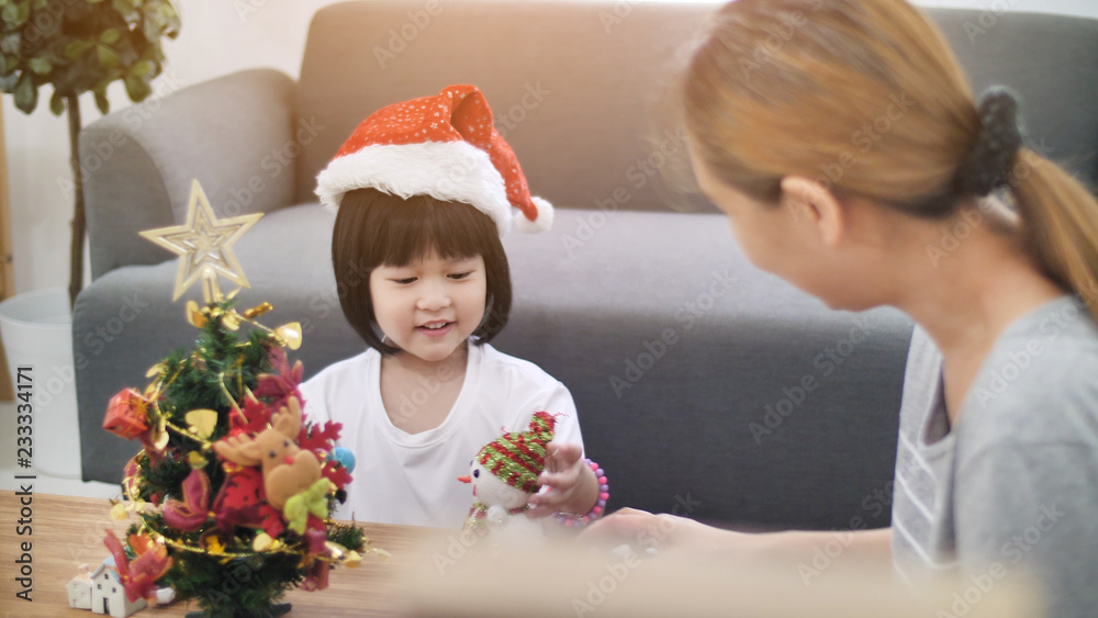 快乐可爱的亚洲女孩和妈妈一起在圣诞树上装饰装饰品