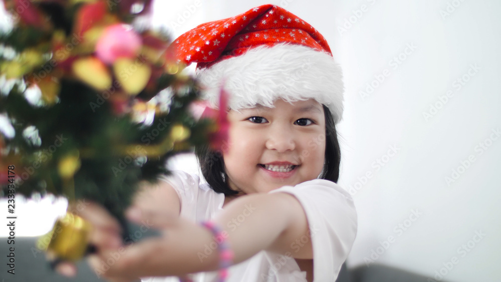 快乐可爱的亚洲女孩把装饰品放在圣诞树上，一起展示