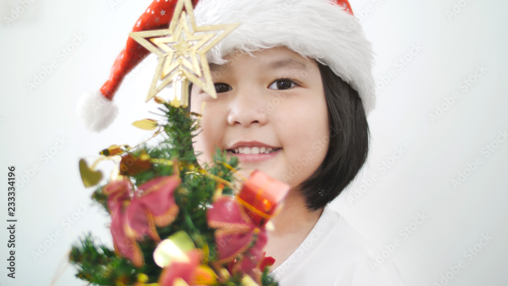 快乐可爱的亚洲女孩把装饰品放在圣诞树上，一起展示