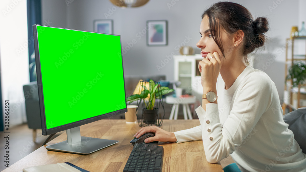 美丽的年轻女孩坐在办公桌前，在绿色实体屏幕个人电脑上工作