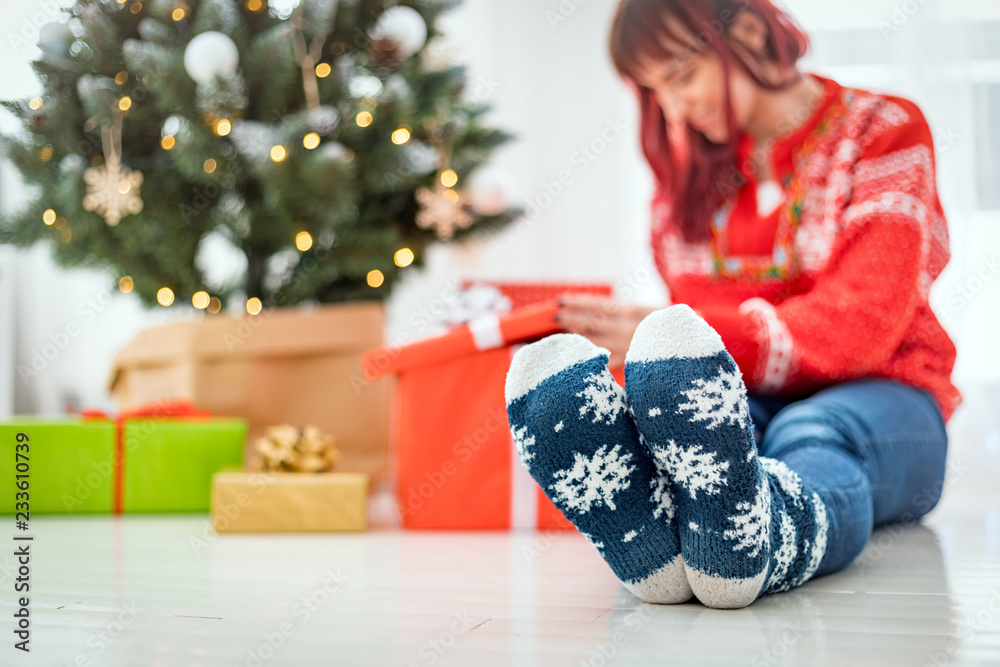 穿着羊毛袜的脚在圣诞树旁，女人在看礼盒