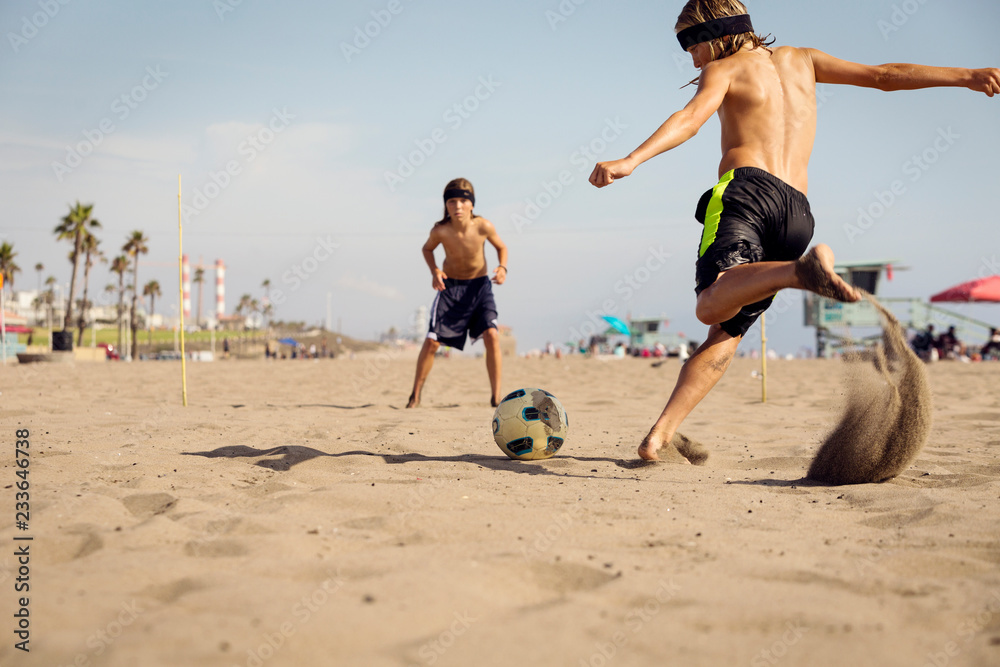 男孩们在海滩上踢足球对抗天空