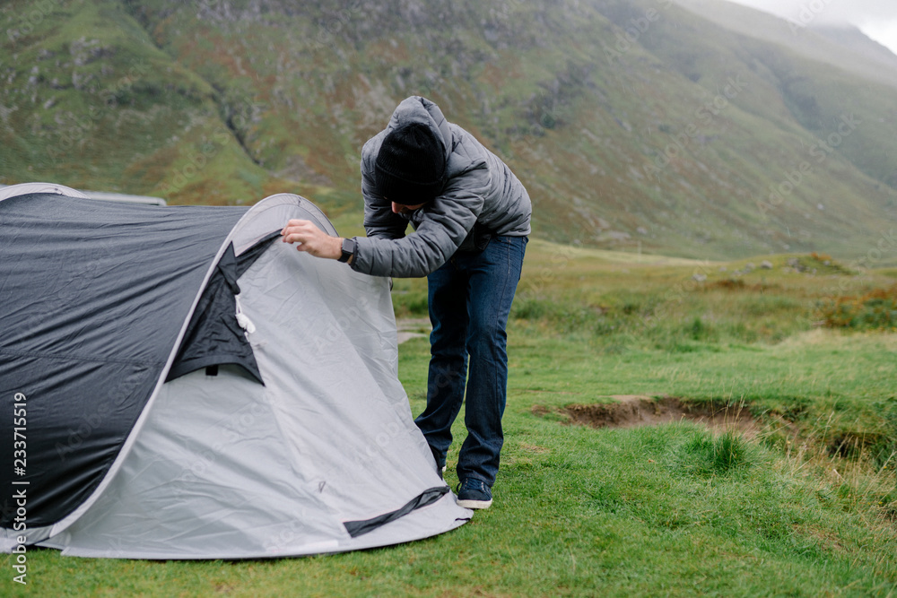 一名男子在下雨时拉着帐篷的拉链