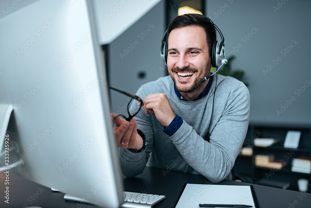 快乐的商务人士，在工作场所对着电脑戴着耳机。