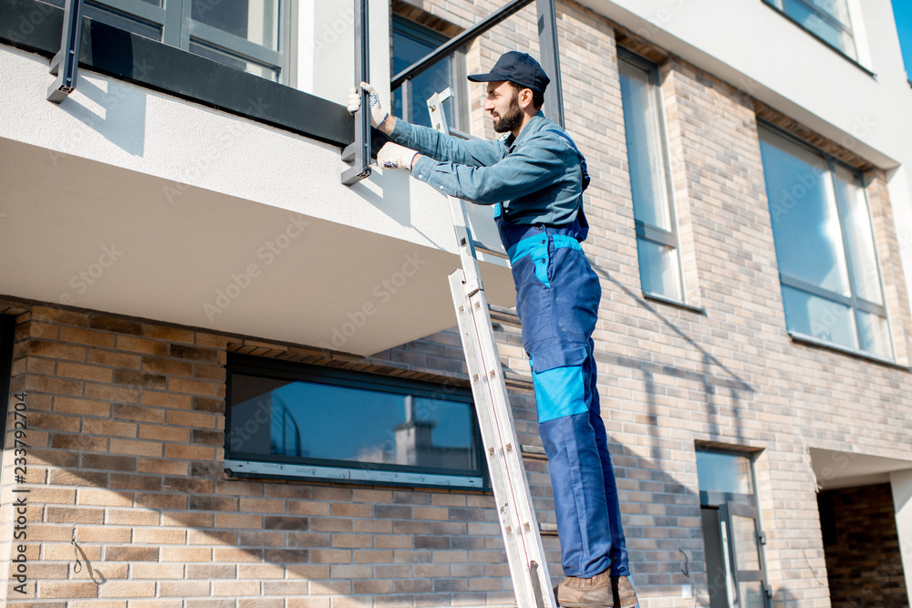 蓝色建筑工人在新建筑的阳台上统一安装铝栅栏