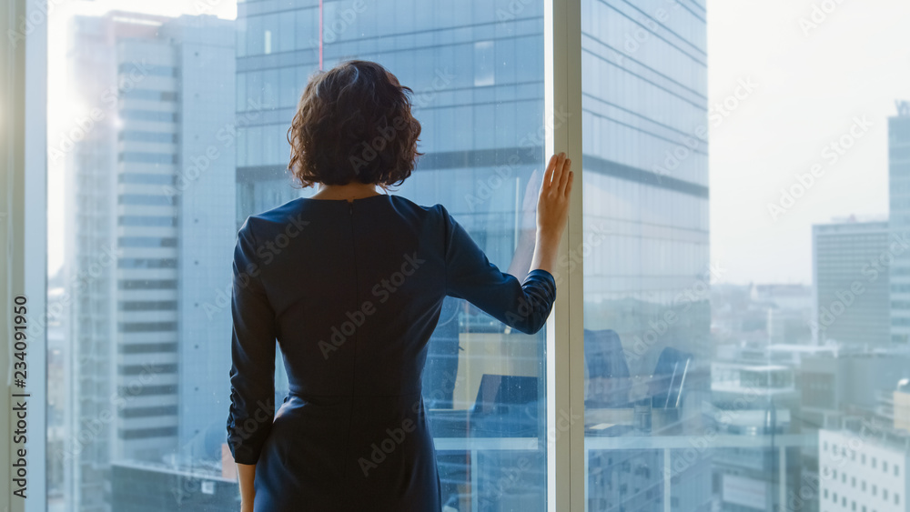 一位成功的女商人穿着引人注目的黑色连衣裙在办公室里眺望窗外的照片