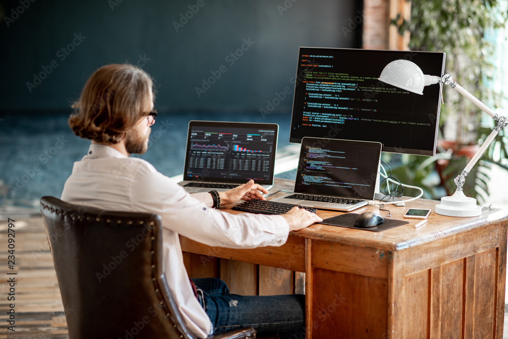 年轻的男性程序员坐在工作场所写程序代码，三台显示器都关着