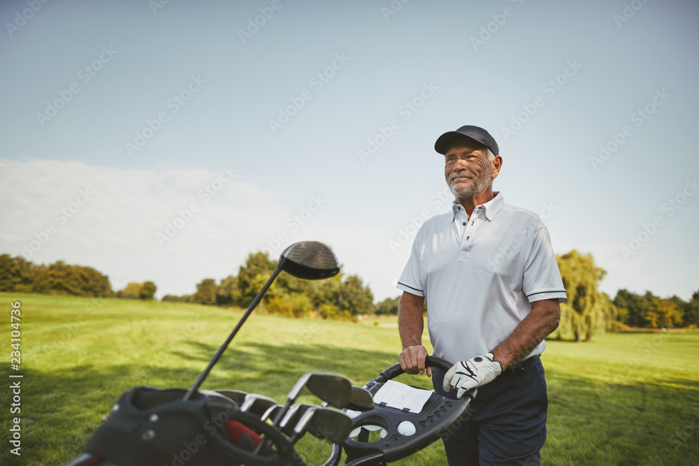 Smiling senior man pushing his clubs on a golf course