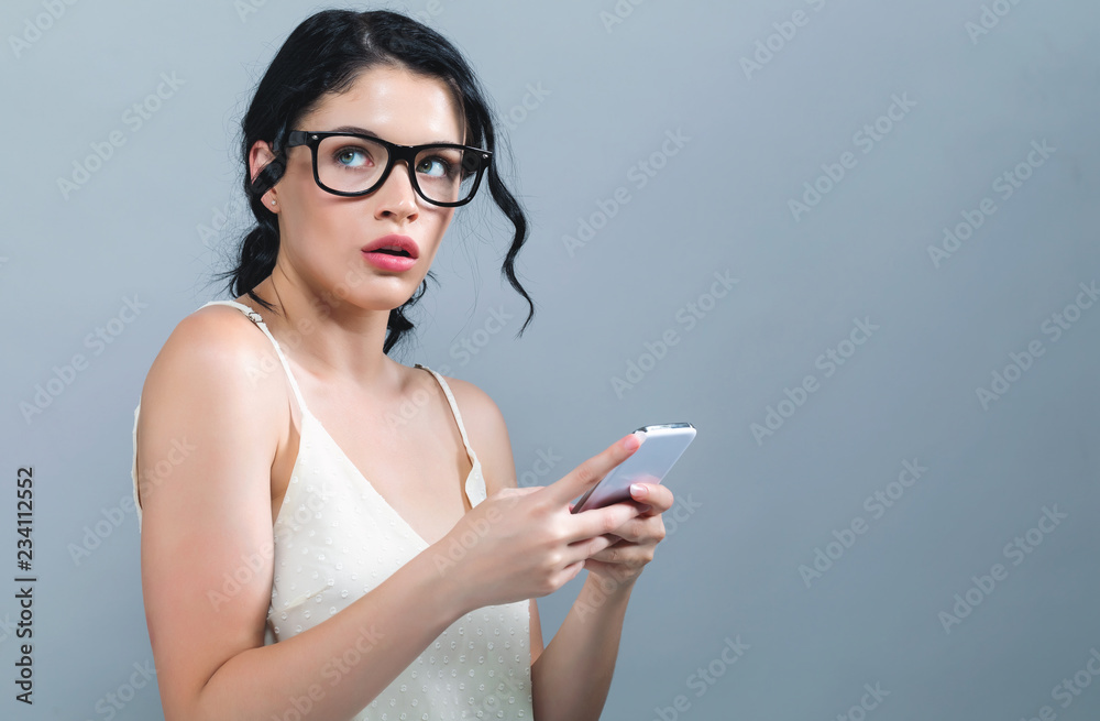 一名年轻女子在灰色背景下盯着手机