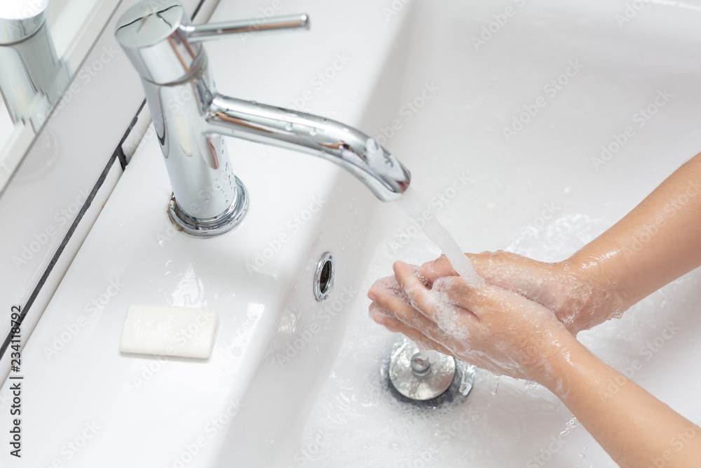 孩子在一个白色的盆里用一块白肥皂洗手。
