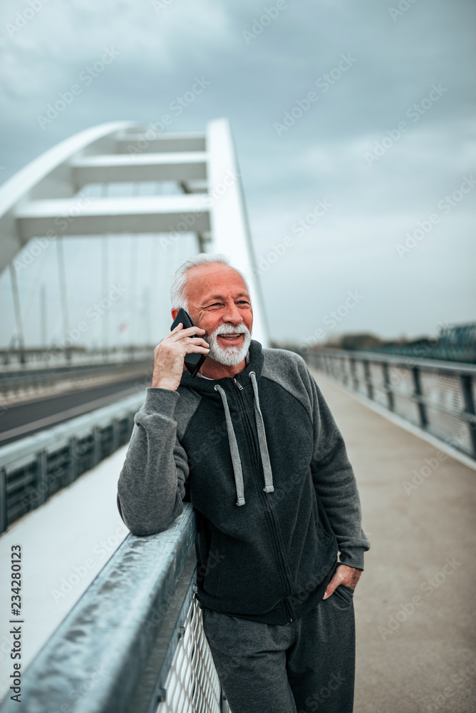 Senior man in tracksuit talking on the smartphone on the city bridge.