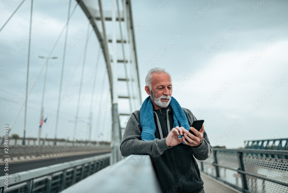 满意的年长英俊男子在外面锻炼后看着手机。