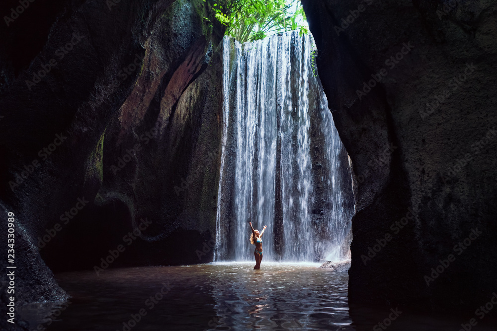 Woman stand in underground cave pool under falling fresh water of Tukad Cepung waterfall. Nature day