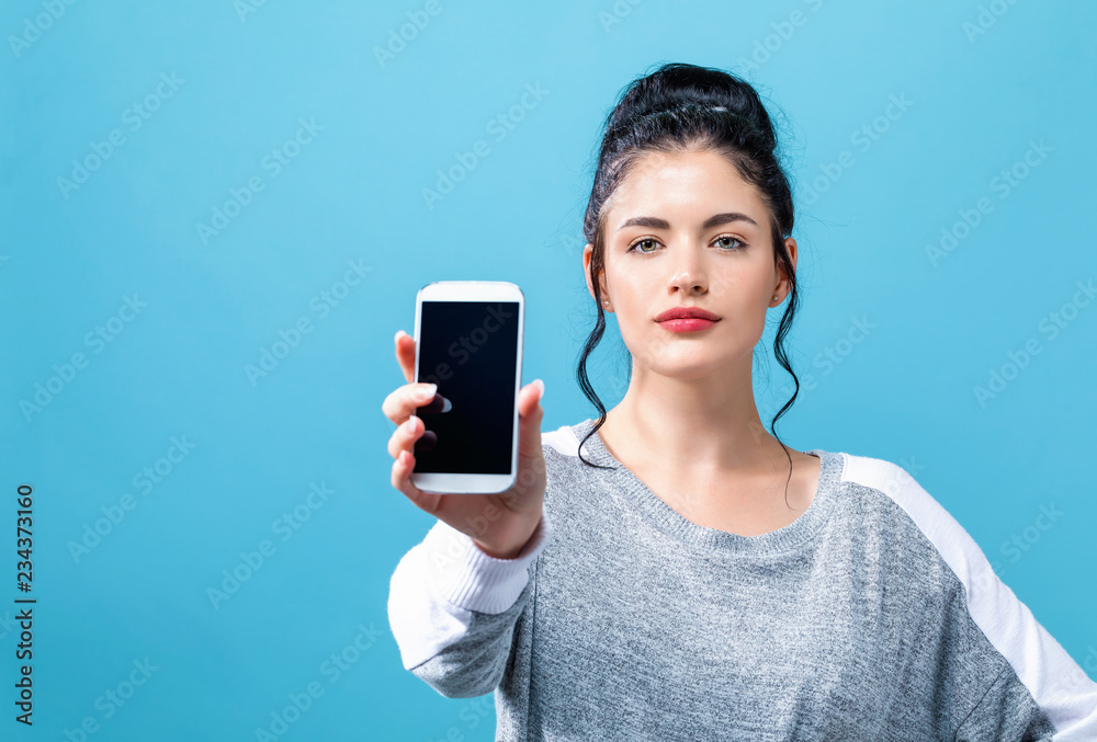 一名年轻女子在蓝色背景下手里拿着一部手机