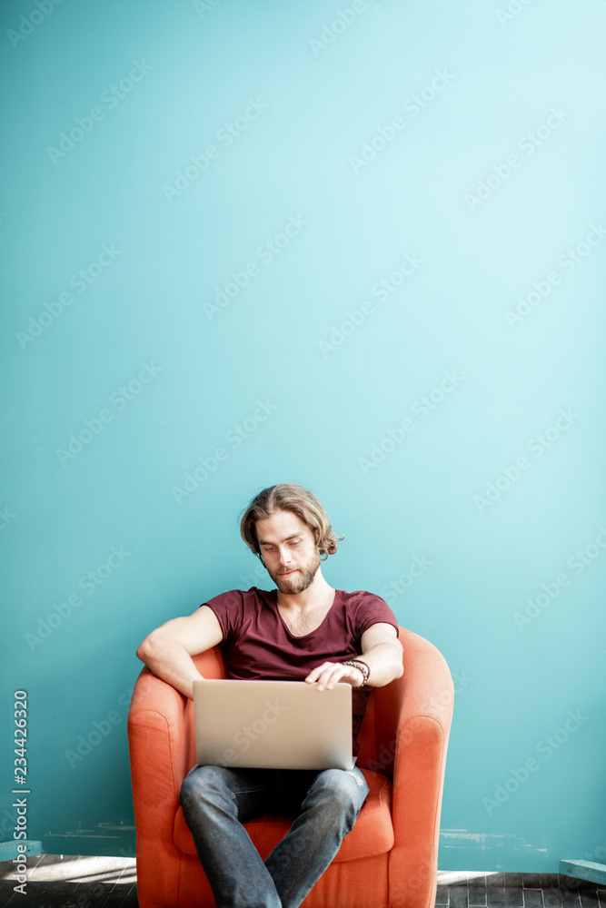 一个留着大胡子、留着长发、穿着t恤、拿着笔记本电脑工作的年轻高加索男子的肖像