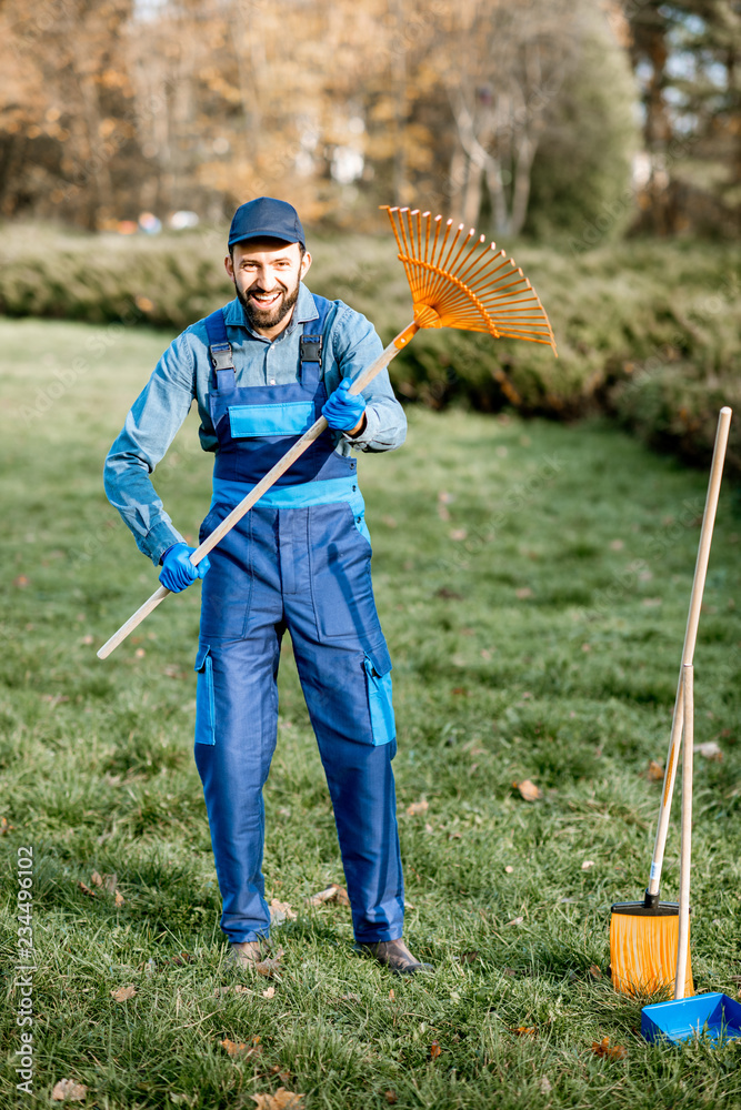 一个穿着制服的男性清扫工或园丁拿着耙子站在花园里的有趣画像