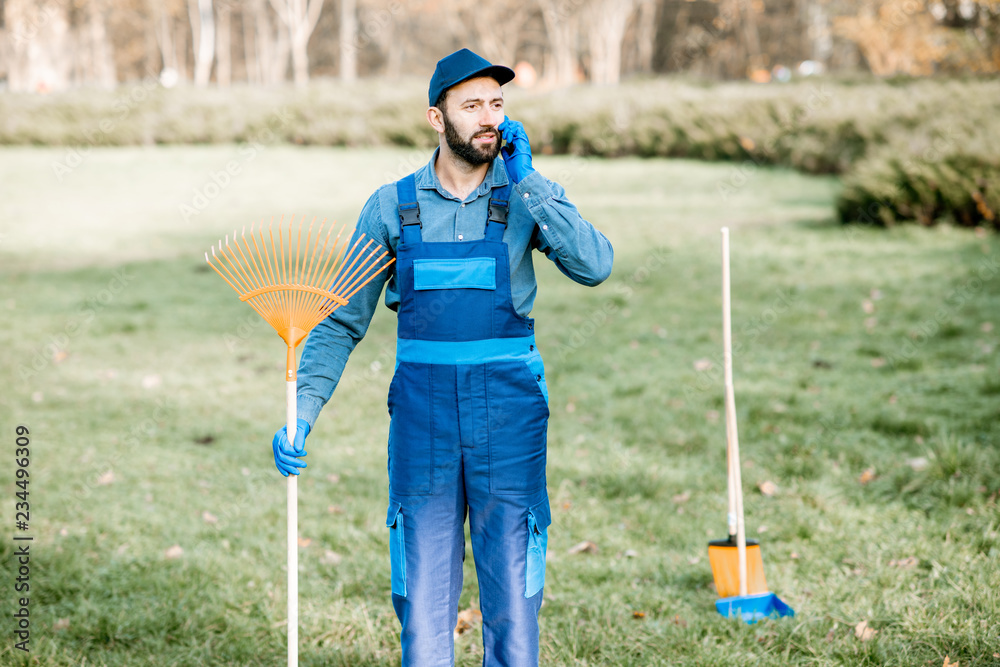 穿着制服的专业清洁工在花园里工作时使用电话