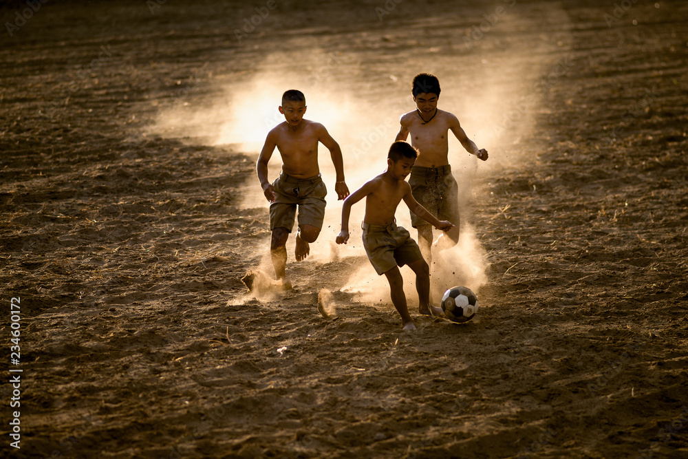 亚洲男孩朋友在夏日阳光明媚的红土地上踢足球。概念友谊和r