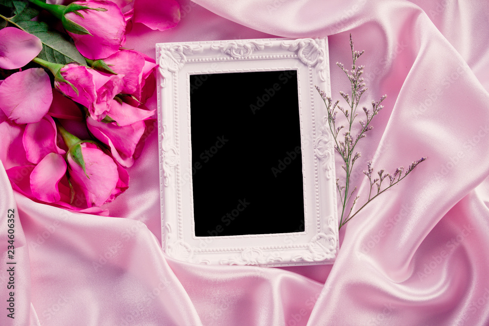 空相框，柔软的粉色丝绸面料上有一束甜美的粉色玫瑰花瓣，浪漫而爱