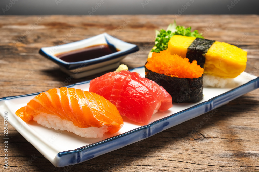 寿司三文鱼、金枪鱼、寿司虾和芥末放在白色盘子里。放在木桌上