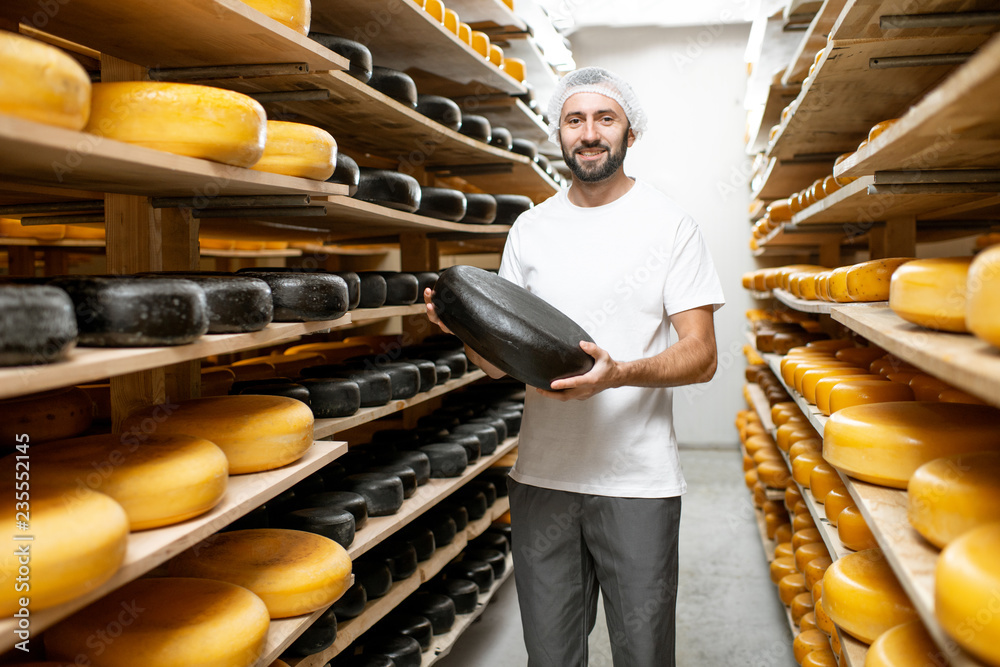 工人在仓库里拿着覆盖着黑蜡的奶酪轮，货架上摆满了奶酪。