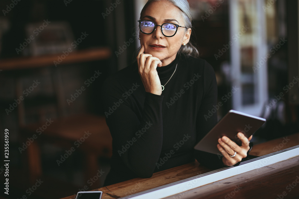 带着数字平板电脑坐在咖啡桌上的资深女商人