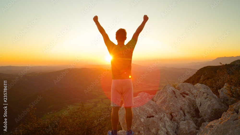 镜头闪光：一个快乐的徒步旅行者在看到日落后举起双臂。