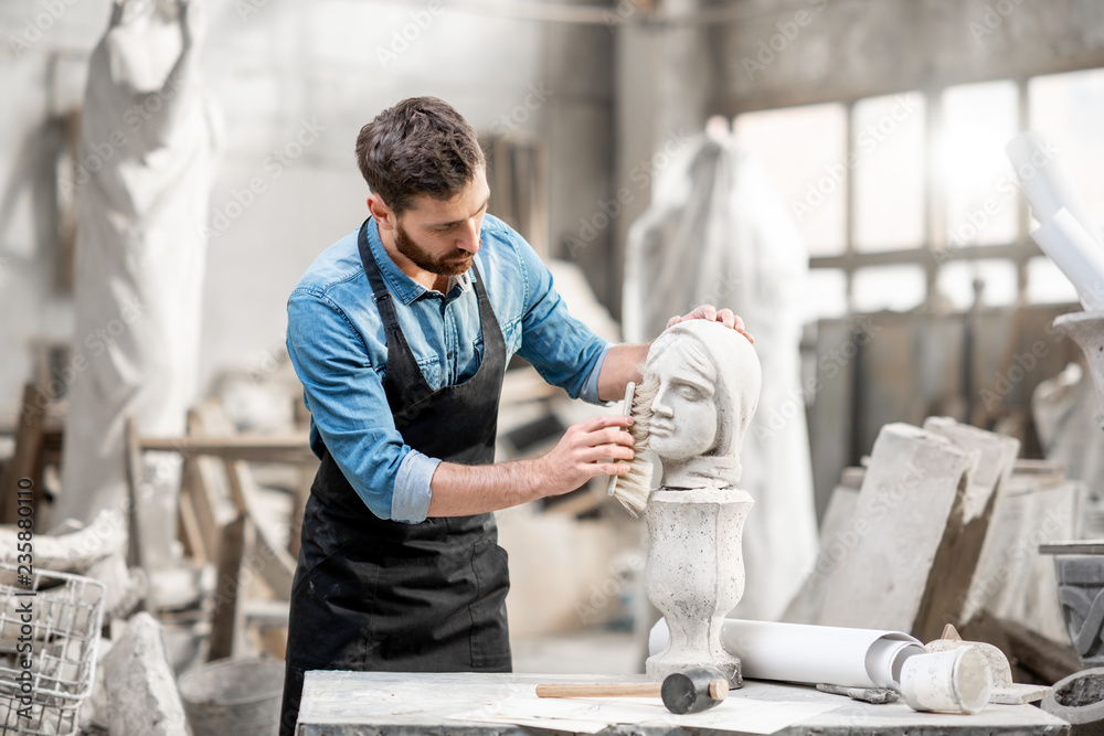 帅气雕塑家在大气工作室的桌子上刷石头头像