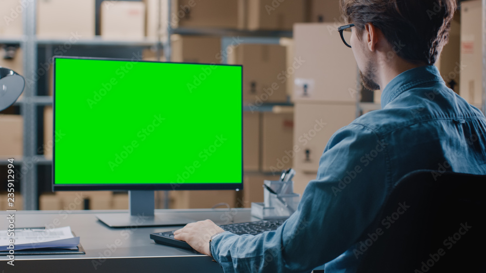 仓库库存经理坐在办公桌前，在绿色实体屏幕电脑上工作
1149552394,仓库库存经理坐在他的Des工作时在个人电脑上使用电子表格