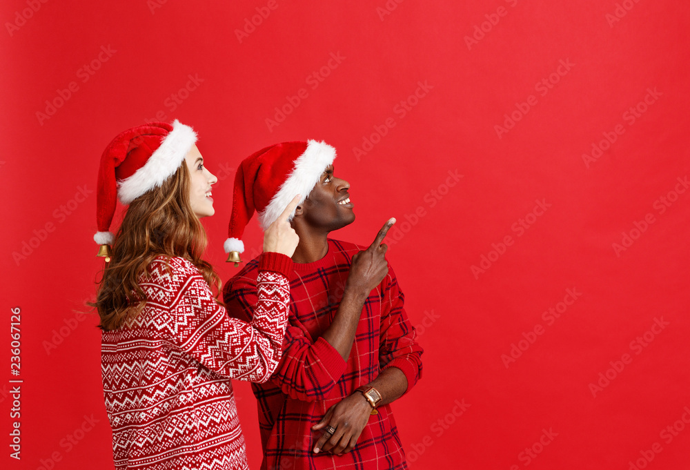 happy couple black man and caucasian woman in christmas hats on red background
